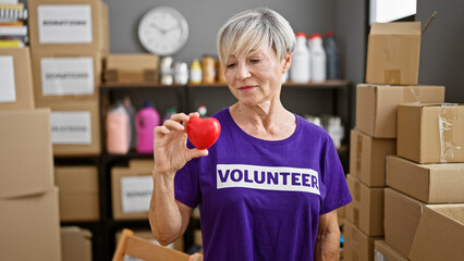 Mature woman volunteer holding a heart in a warehouse full of donation boxes.