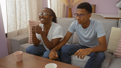 Happy african american mother and son sitting on a couch in the living room at home, sharing a joyful moment together indoors