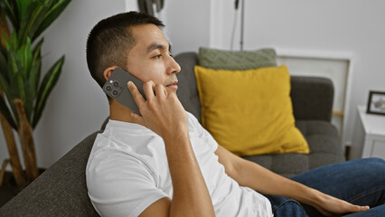 Young hispanic man talking on the phone in a modern living room.