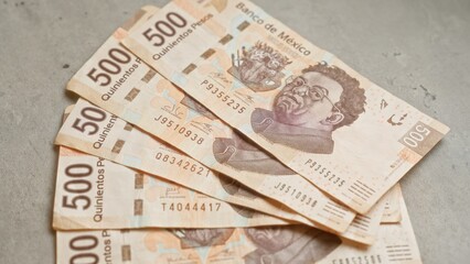 Mexican 500 pesos banknotes are laid out on a concrete surface displaying their design prominently.