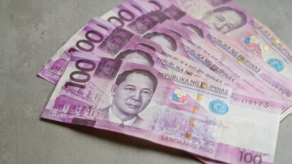 Philippine pesos banknotes on a concrete surface showcasing 100 peso bills in a fan arrangement.