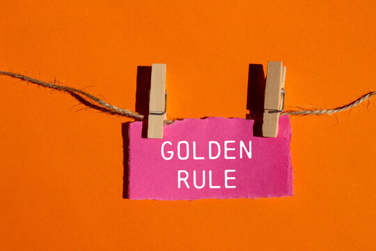 Golden rule message written on ripped torn pink paper piece with orange background. Conceptual golden rule symbol. Copy space.