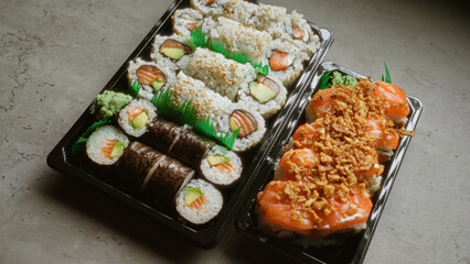 Fresh assorted sushi rolls in black plastic trays placed on a grey concrete surface