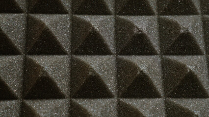 Closeup of black acoustic foam panels with a textured surface arranged in a pattern for soundproofing and noise reduction in a studio or recording environment