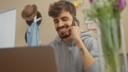 Bearded hispanic man smiling in apartment while talking on smartphone