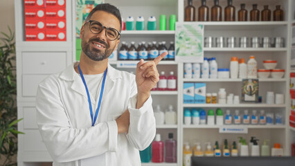 A confident hispanic man pharmacist gestures in a well-stocked pharmacy interior.