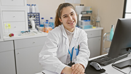 Smiling young hispanic woman in a white lab coat working at a hospital laboratory with a computer