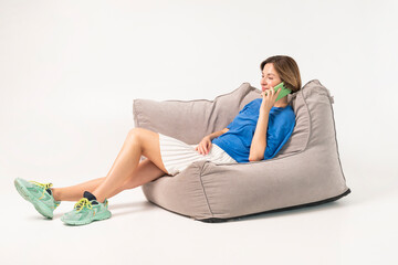 Beautiful girl sitting on poof and talking on phone isolated on white background