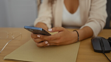 Woman using smartphone at office desk with document and computer mouse