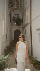 A young hispanic woman strolls through the beautiful streets of the old town in locorotondo, puglia, italy, admiring the charming white buildings and vibrant potted plants.