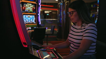Focused young woman playing slot machine at a casino lit with neon lights.
