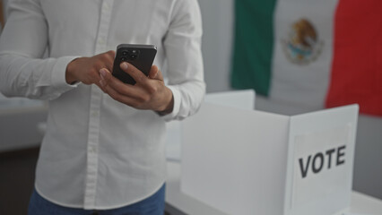 Young hispanic man using smartphone in mexican voting room with flag