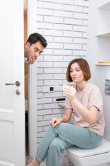 Young excited woman sitting in the restroom and demonstrating to her husband the positive result of pregnancy test