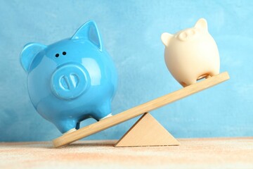 Financial inequality. Piggy banks of different size showing imbalance on scales against light blue...