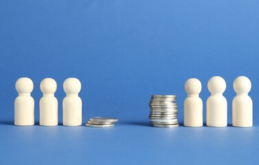 Financial inequality. Wooden figures and stacked coins of different height against blue background