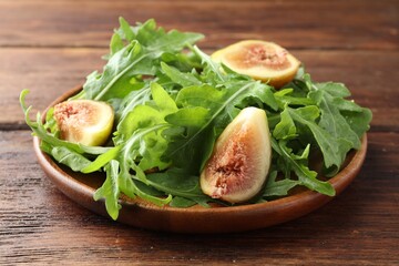 Fresh arugula and cut fig on wooden table, closeup