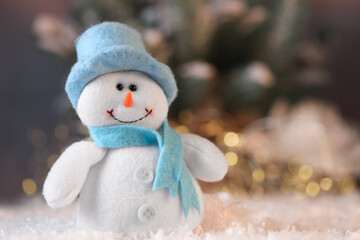 Funny snowman figure on artificial snow against blurred lights, closeup