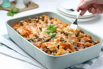 Woman eating delicious al forno pasta at white table, closeup