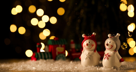 Cute decorative snowmen on artificial snow against blurred lights. Space for text