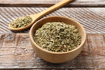 Dried oregano in bowl and spoon on wooden table, closeup