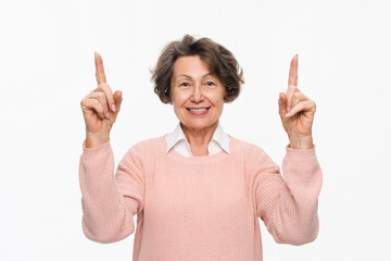 Cropped portrait of elderly woman in casual clothes pointing upwards on copy space isolated over white background. Senior Caucasian grandmother showing empty space closeup