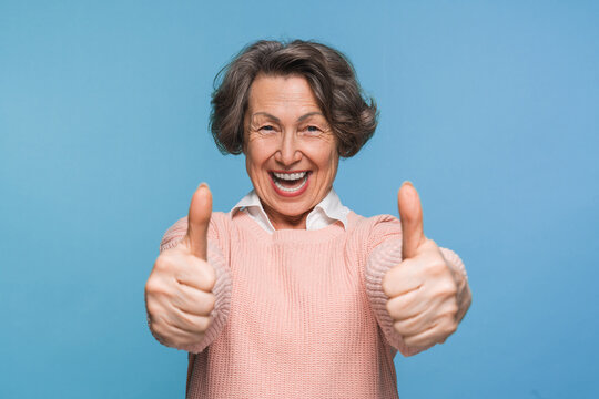 Mature satisfied happy smiling caucasian woman female pensioner in casual clothes showing two thumb up like gesture isolated on blue color background studio portrait. People lifestyle concept