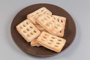 Flat flaky cookies on a brown dish on gray background