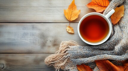 A cup of tea with autumn yellow leaves and a scarf on a wooden table, top view.