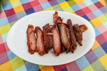 close up of Chinese Cantonese barbecued grilled Char Siu pork on a white plate with colourful table cloth