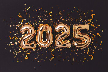2025 New Year concept. Golden foil balloons, ribbons and confetti on a black background.