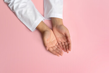 The hands of a female doctor in a white coat, palms up, lie on the table on a solid pink background...