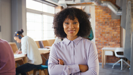 Portrait Of Smiling Businesswoman Working In Busy Open Plan Office With Colleagues In Background