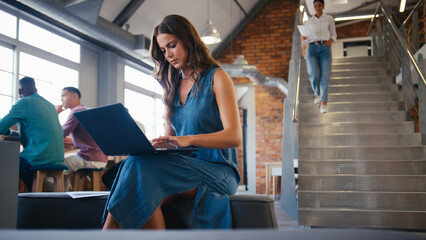 Young Businesswoman Sitting And Working On Laptop In Busy Modern Open Plan Office 