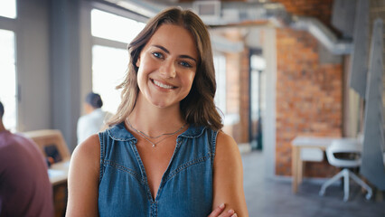 Portrait Of Smiling Young Businesswoman Working In Open Plan Office With Colleagues In Background