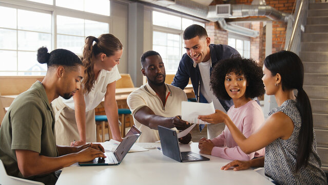 Multi-Cultural Business Team Meeting Around Desk In Modern Open Plan Office Discussing Documents