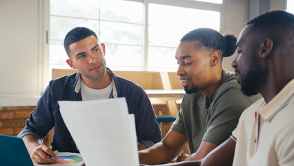 Three Young Businessmen Meeting In Modern Office Sitting Around Table Working On Laptop Together