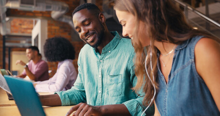 Male And Female Businesspeople Meeting In Office Working On Laptop With Colleagues In Background