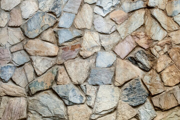 old stone fence made of gray and brown cobblestones, uneven stones close up