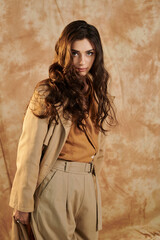 Fototapeta premium A young woman elegantly poses in a trendy autumn outfit, exuding style and grace against a textured background.