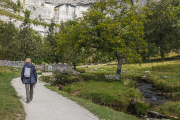 A senior walks along the path towards the iconic limestone face of Malham Cove one of the highlights of any visit to the Yorkshire Dales