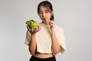 Portrait of a happy playful Asian girl eating fresh salad from a glass bowl after workout at home. Young lady Enjoying Healthy Nutrition And Organic Food, Having Vegetarian Meal