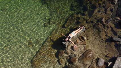 Woman sunbathing on a rock in the middle of crystal-clear waters