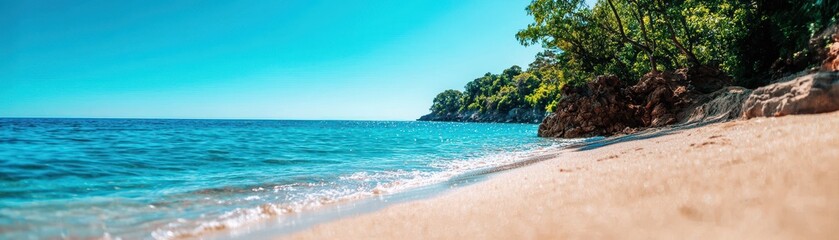 Obraz premium Tropical beach with white sand and clear blue water, surrounded by lush green trees under a clear sky. Ideal summer vacation spot.