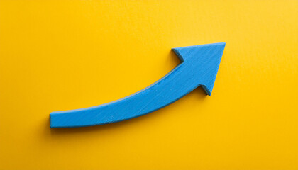 Blue wooden arrow pointing upwards on yellow background. Business and market growth. Flat lay