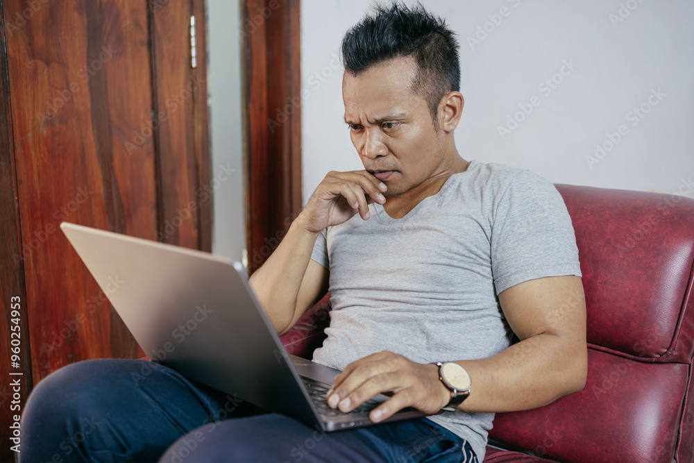 Wall mural serious asian man work on computer laptop while stay at home.