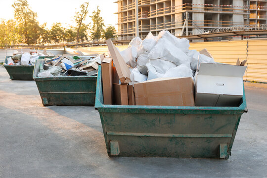 Garbage cans stand next to a house under construction at sunset. Container with construction debris.