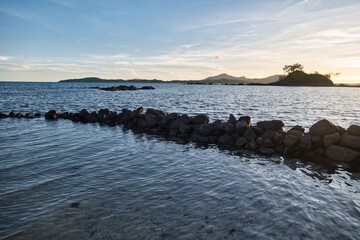 A row of stones in the water in front of a bright sunset sky over deep blue water. Peaceful sunset scene on the Yasawa Islands, Fiji. Small islands during sunset. Tiny calm waves and dark silhouettes.