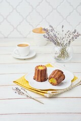 Dessert, canele with lemon curd on a white plate on a light wooden background.