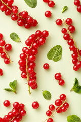 Red currant berries with green leaves on pastel green background viewed from above. 