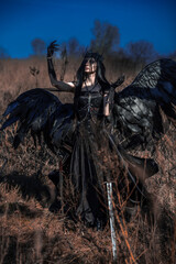 Fototapeta premium Goddess of death with black wings on a dried field